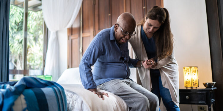 Home caregiver helping a senior man standing up at home